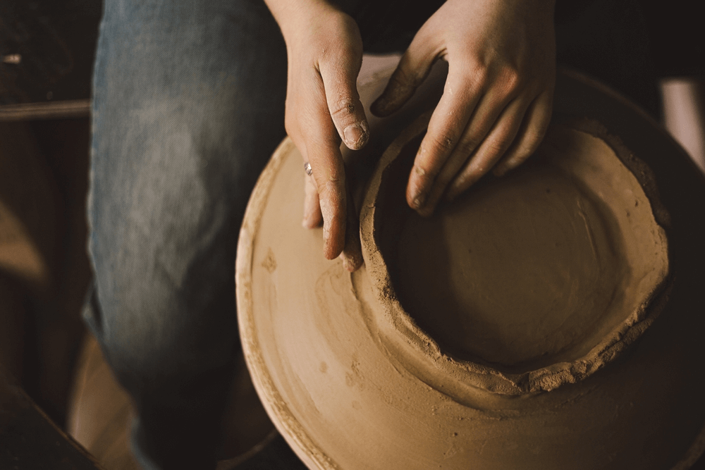 Artisan's hands covered in clay, delicately shaping a pot on a wheel.